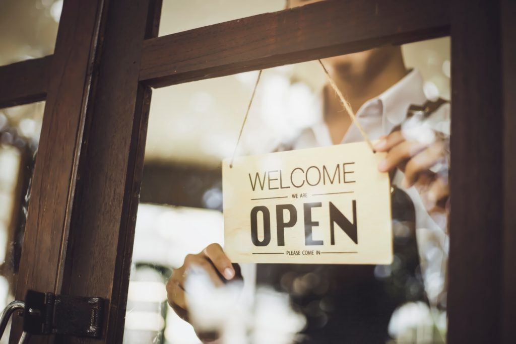 person displaying open store sign in shop window